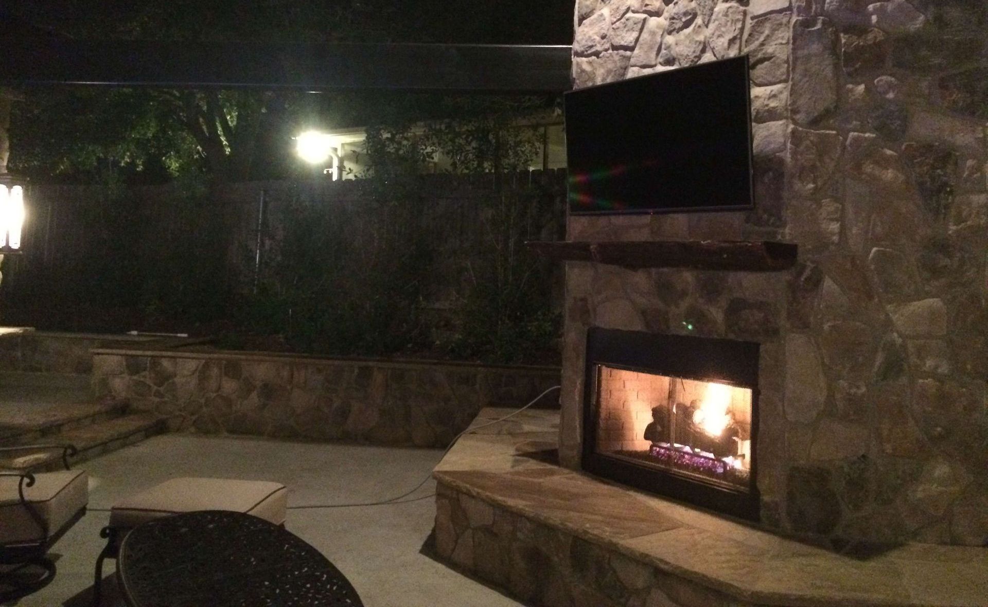 A fireplace is lit up at night in a backyard