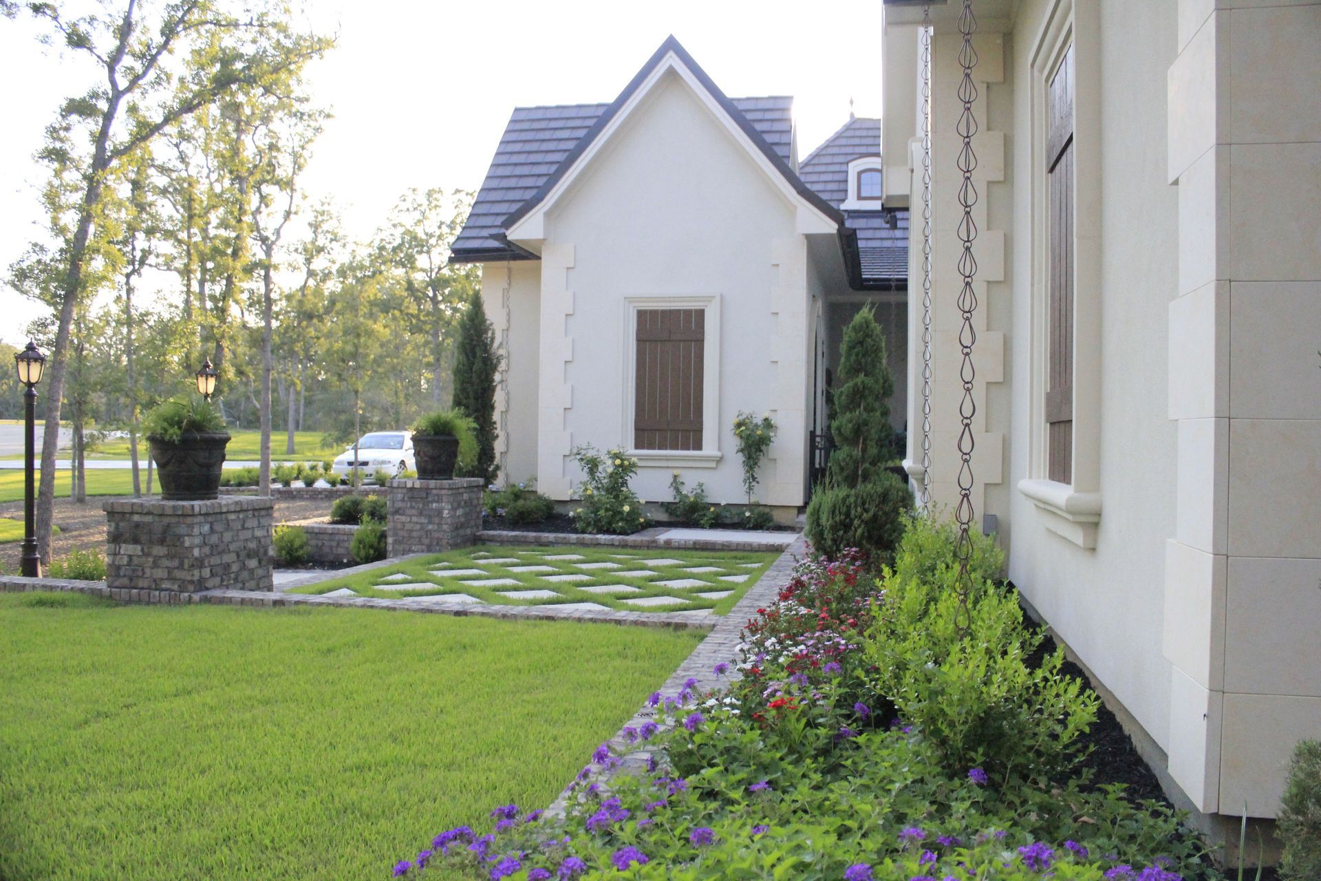 A white house with a black roof and a lush green lawn in front of it.