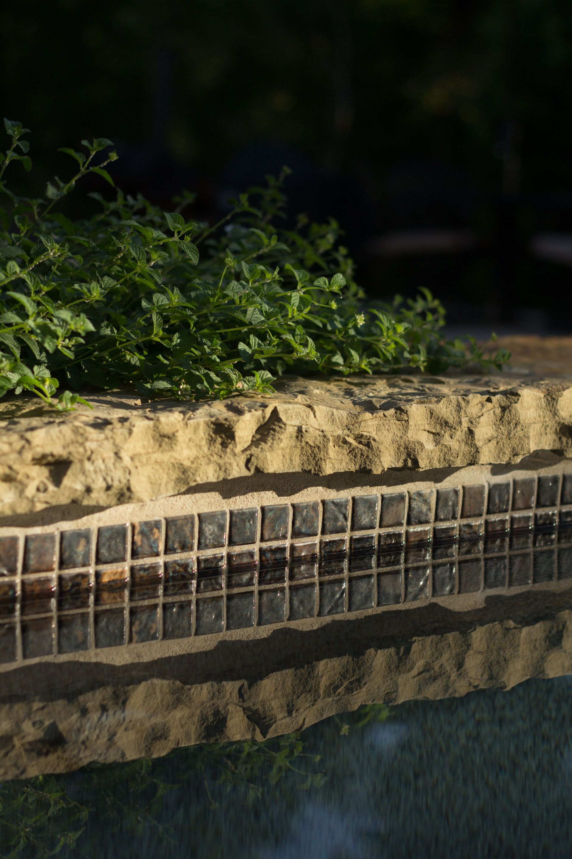 A swimming pool with a stone wall surrounding it and a reflection of the wall in the water.