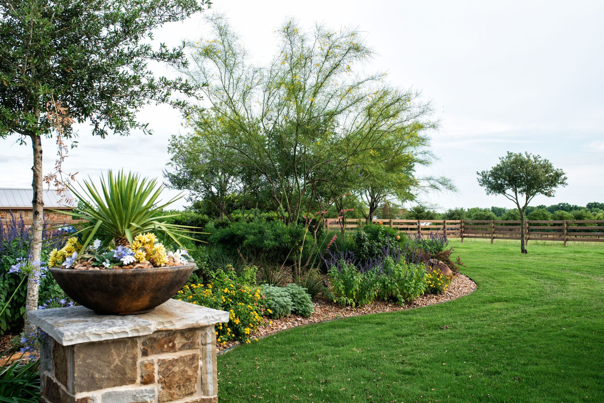 A bowl of flowers is sitting on top of a stone pillar in a garden.