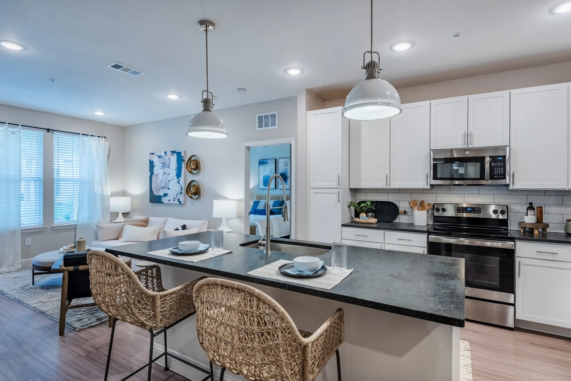 Modern kitchen and living area with island seating and view into bedroom.