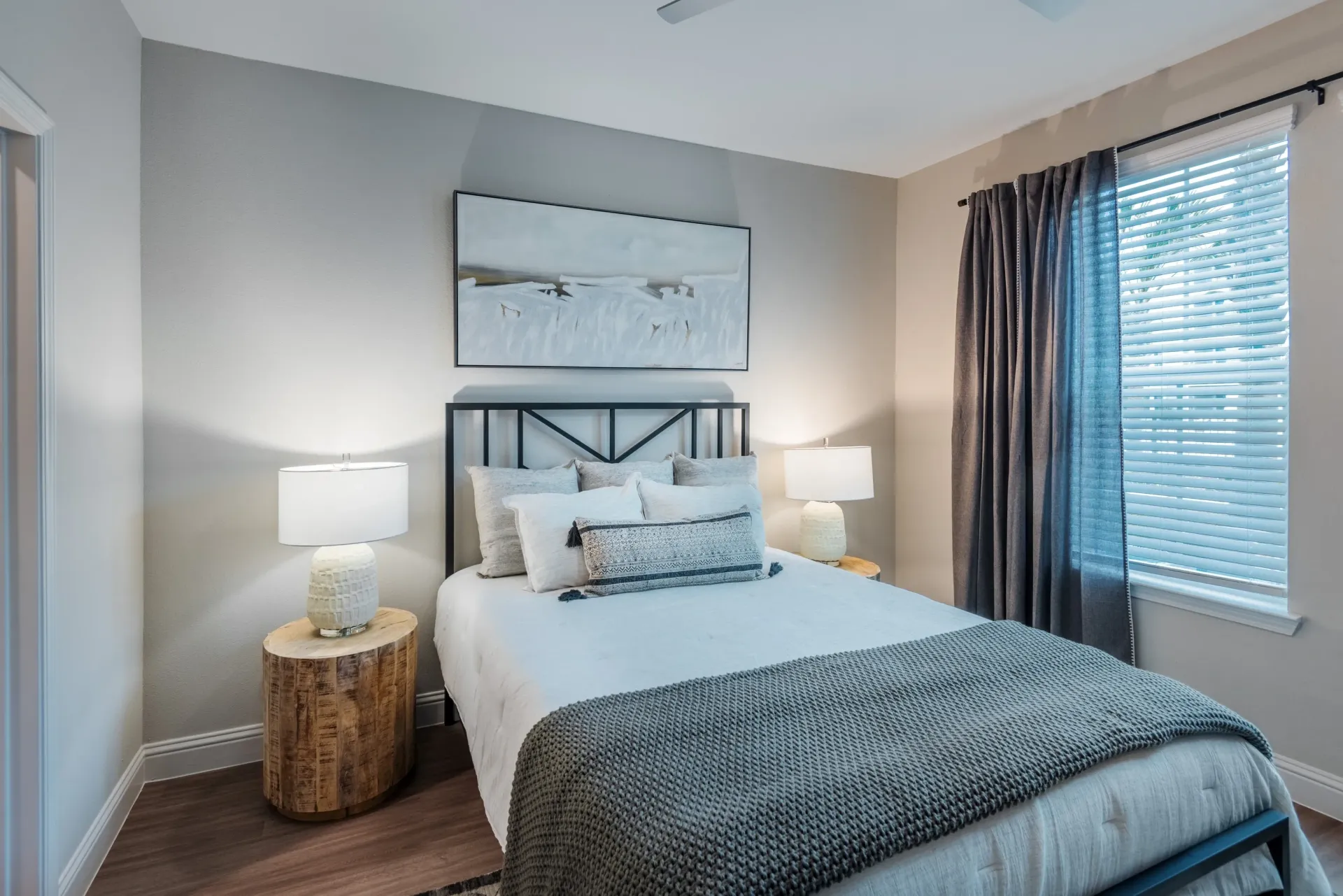 Cozy bedroom with a queen-size bed, modern bedside lamps, and a large window with blinds.