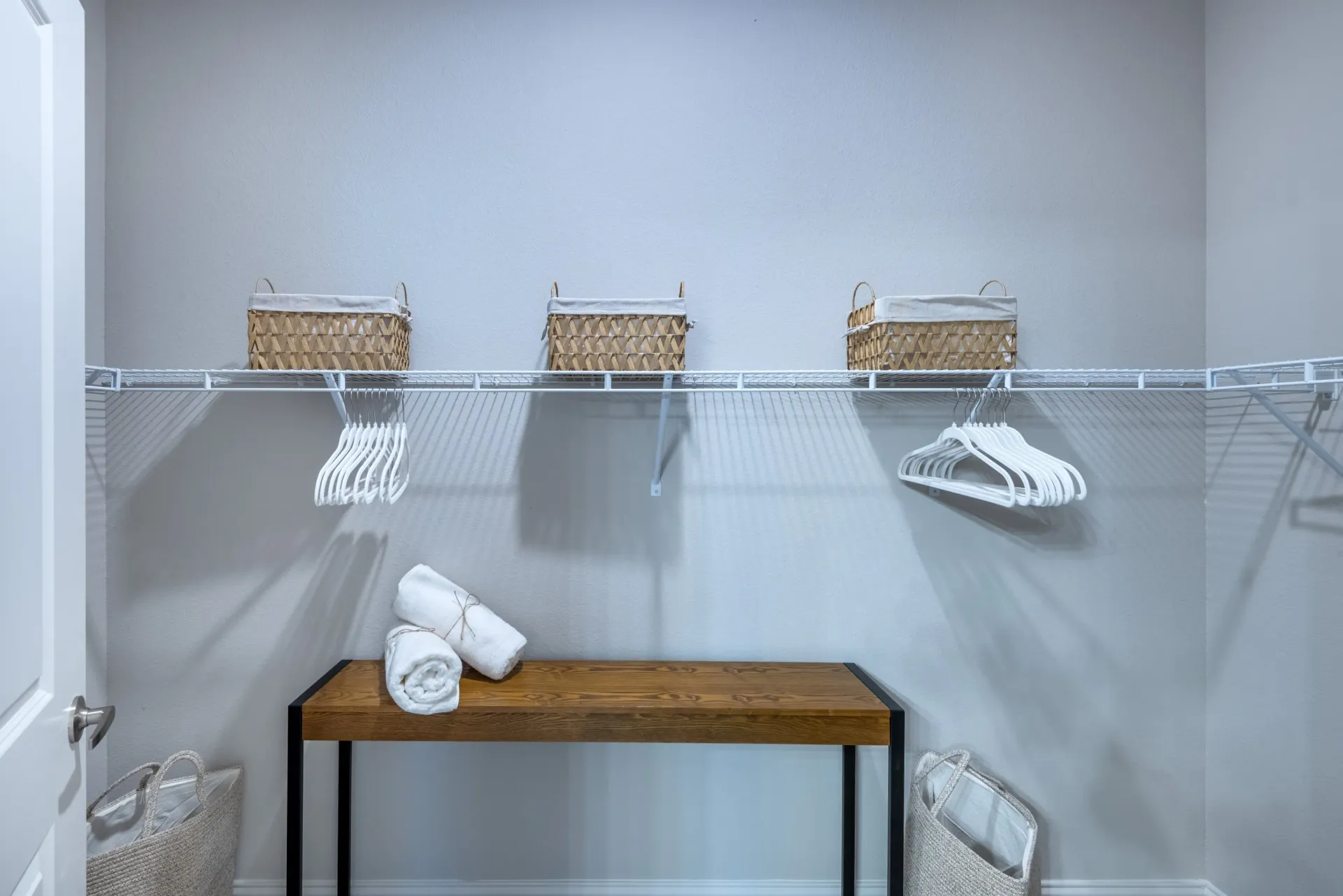Walk-in closet with shelving, baskets, and a bench with rolled towels.