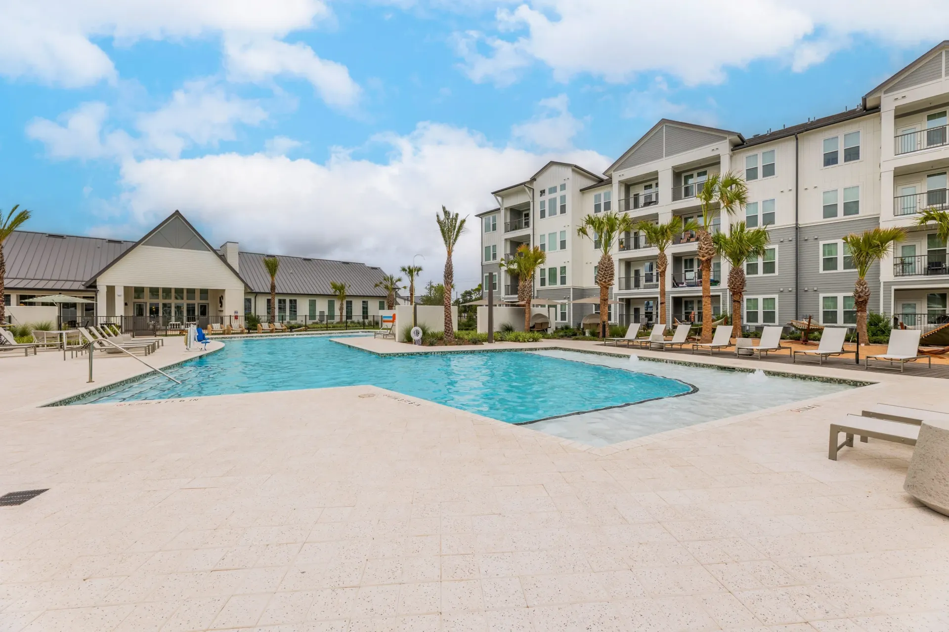 Resort-style swimming pool with lounge chairs and palm trees in front of apartment buildings.