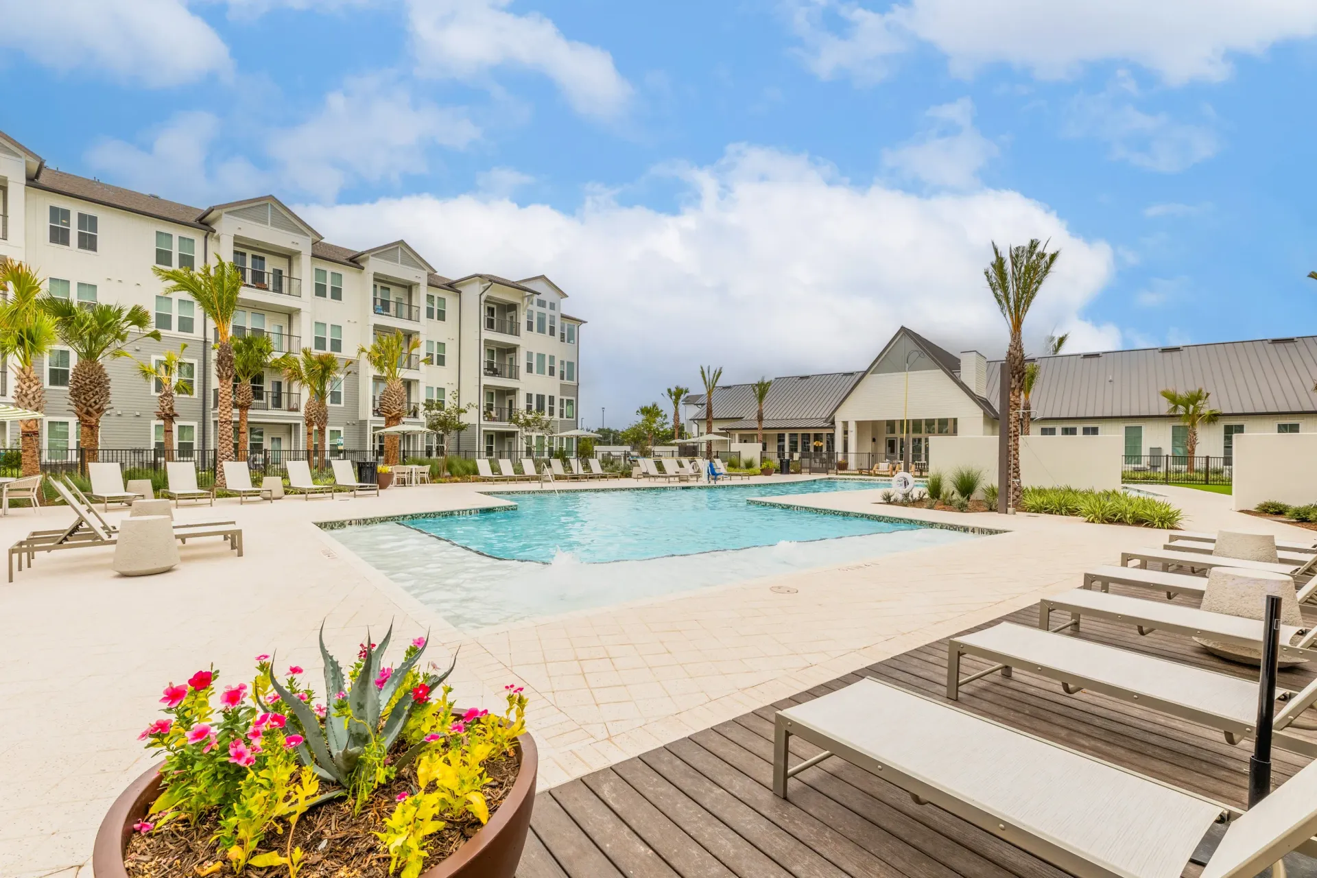 Resort-style swimming pool with lounge chairs and palm trees, adjacent to apartment buildings.