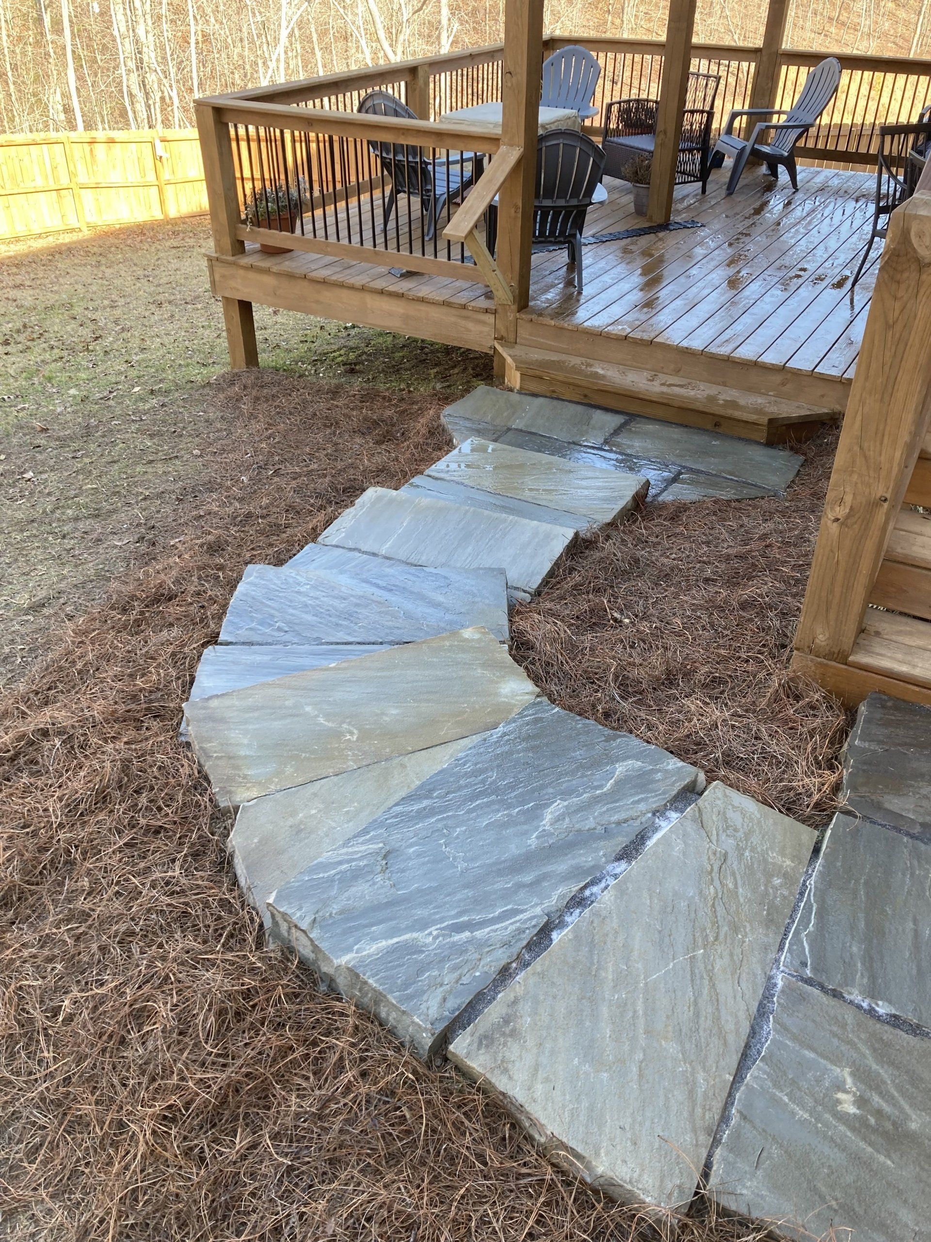 A stone walkway leading to a wooden deck with chairs and tables.