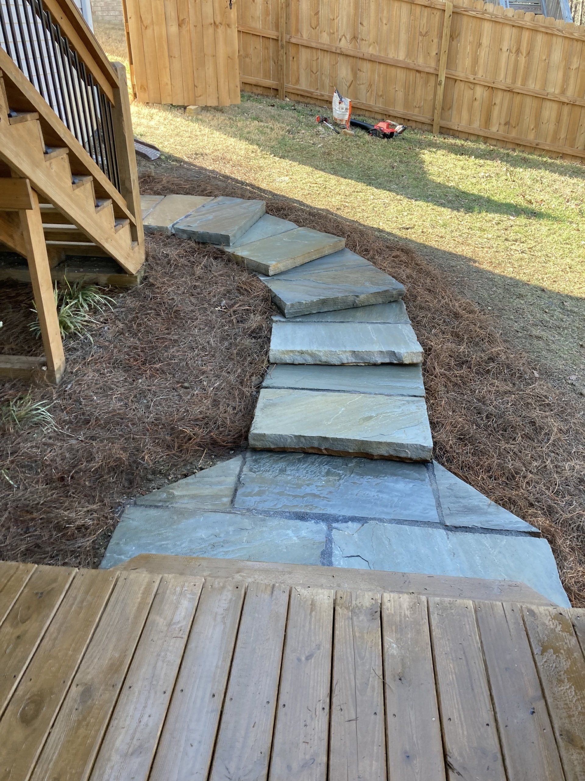 A stone walkway leading to a wooden deck in a backyard.