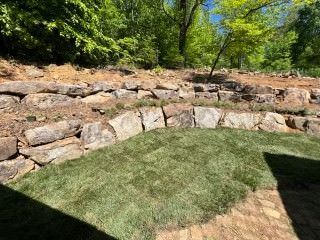 A stone wall is surrounded by grass and trees in a backyard.