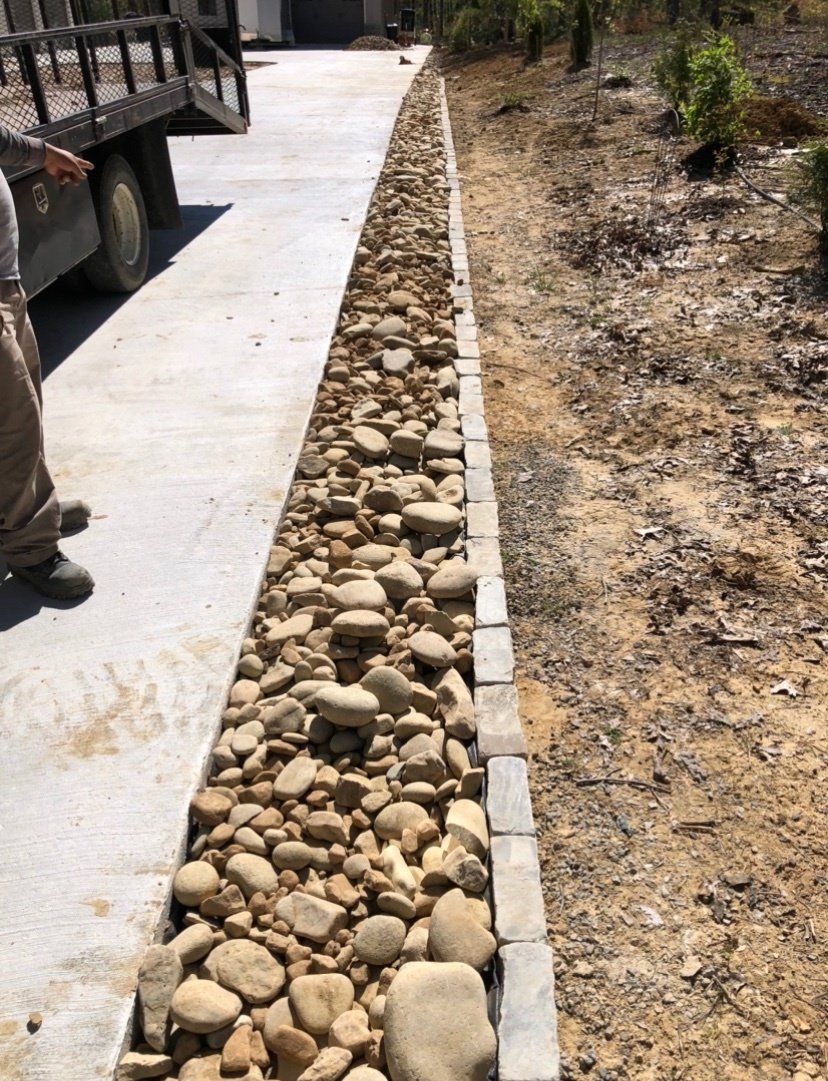 A man is standing next to a row of rocks on the side of a road.