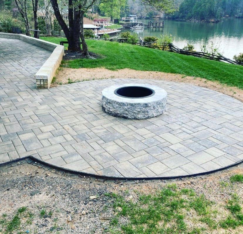 A fire pit is sitting on a brick patio next to a lake.