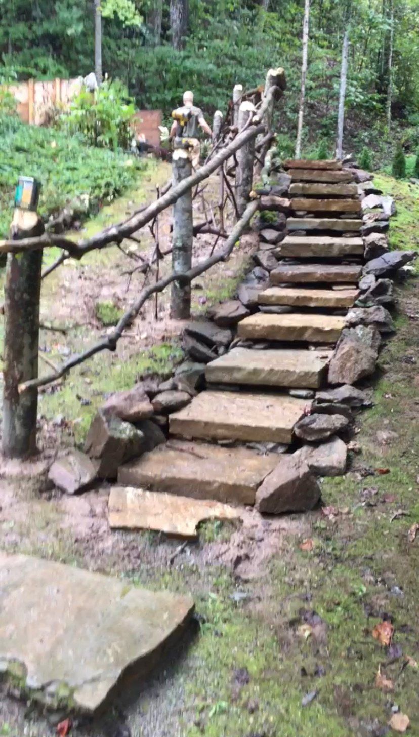 A stone walkway with a wooden railing in the middle of a forest.