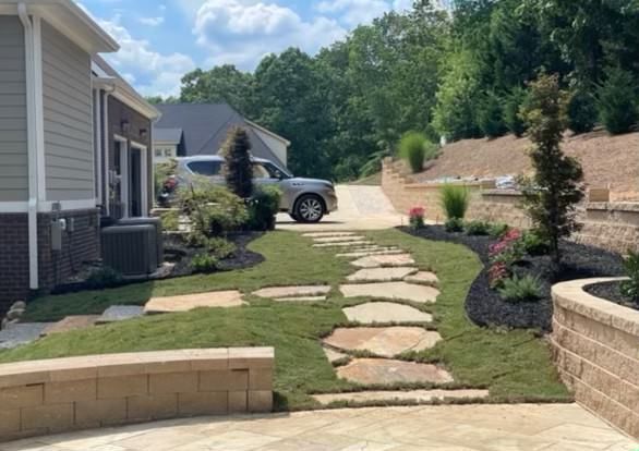 A stone walkway leading to a house with a car parked in the driveway.