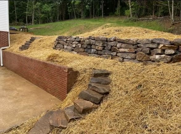 A pile of hay is sitting on top of a hill next to a brick wall.