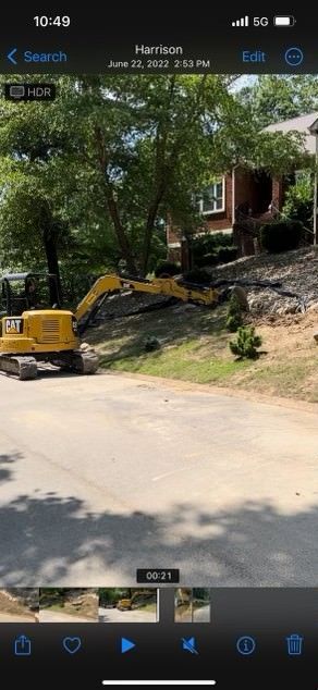 A yellow excavator is sitting on the side of a road in front of a house.