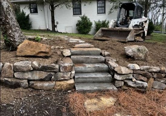 A stone wall with stairs leading up to it and a bulldozer in the background.