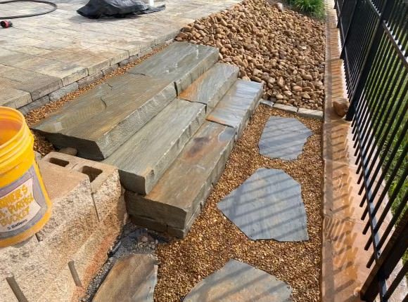 A yellow bucket is sitting next to a stone walkway.
