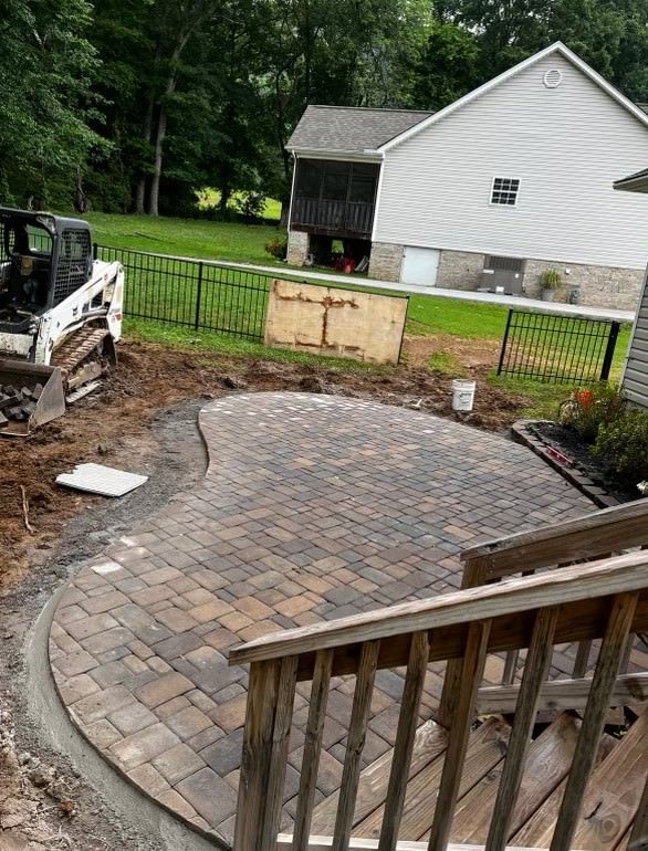 A bobcat is working on a patio in front of a house.
