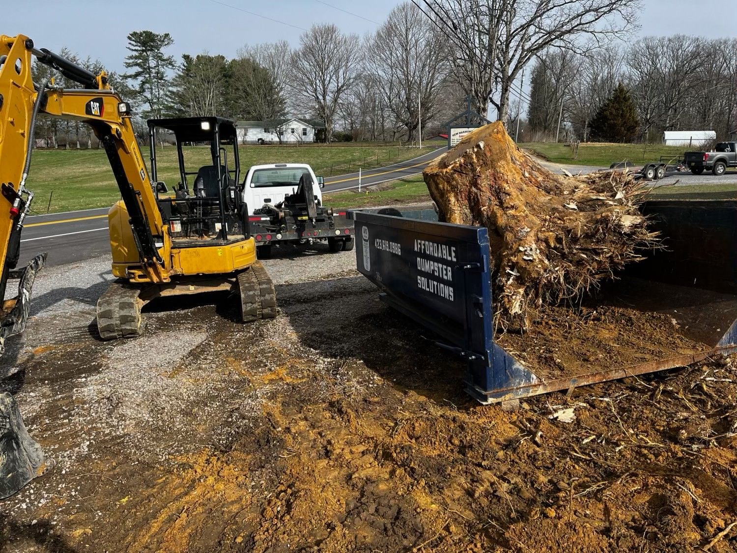 A large pile of dirt is being loaded into a dumpster.