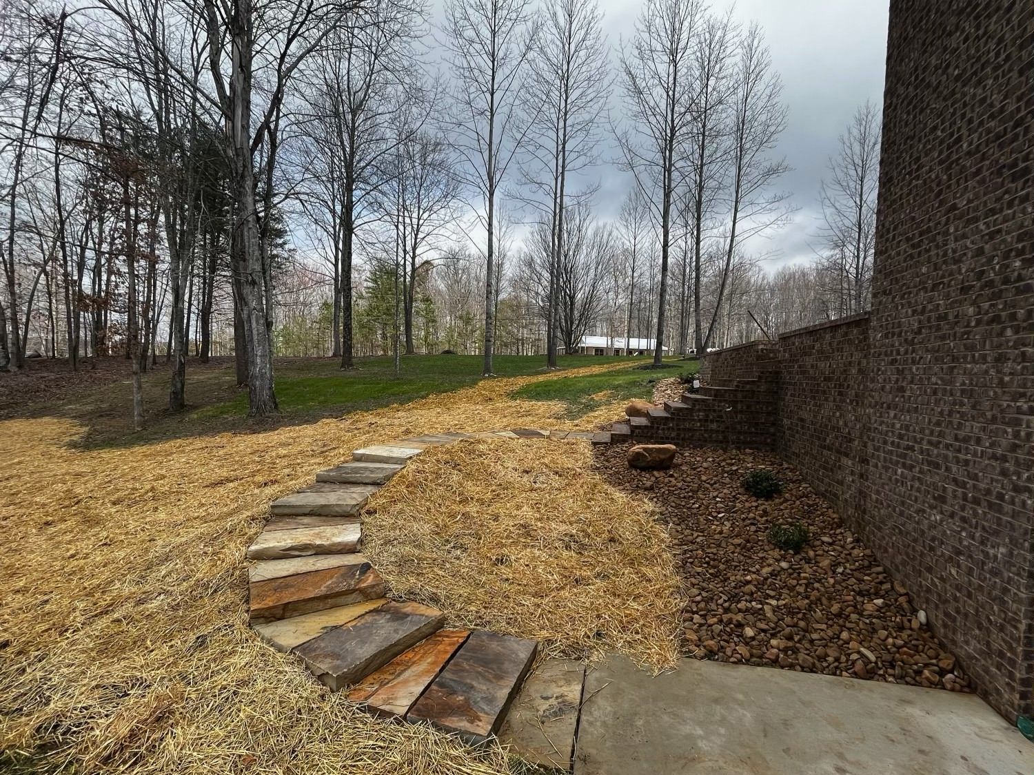 A stone walkway leading to a house with trees in the background.