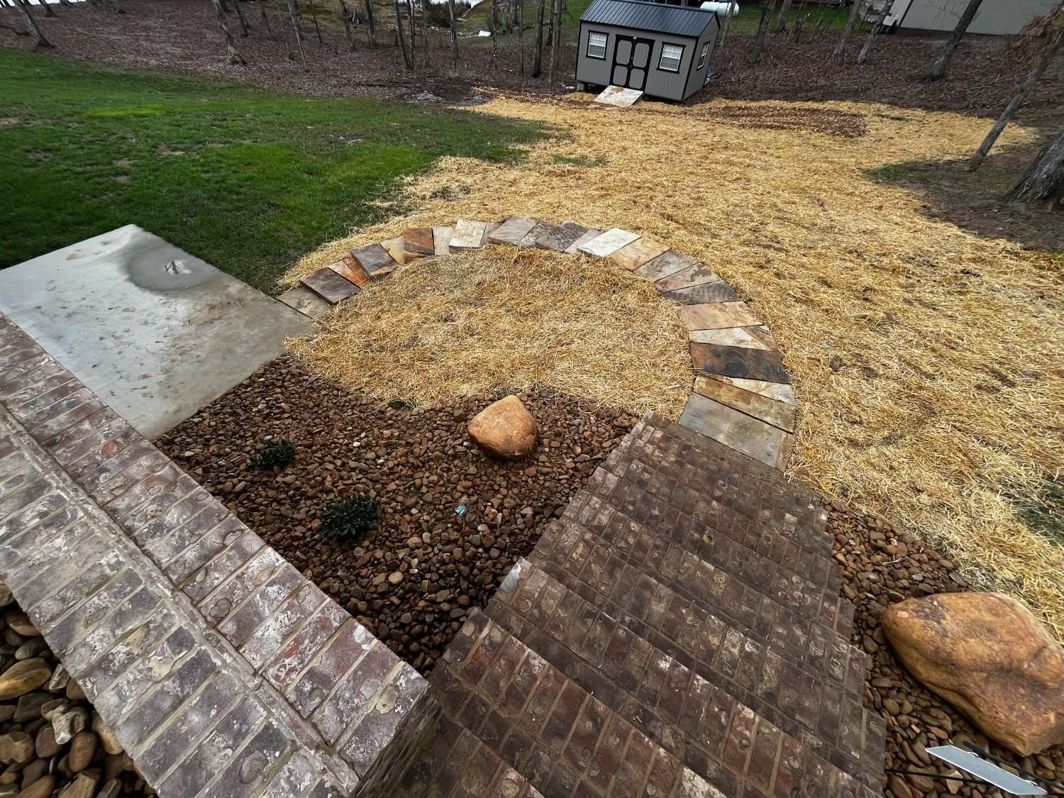 A brick walkway surrounded by rocks and mulch in a backyard.