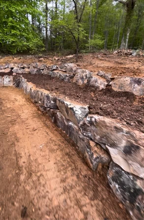 A rock wall is being built in the middle of a dirt road in the woods.