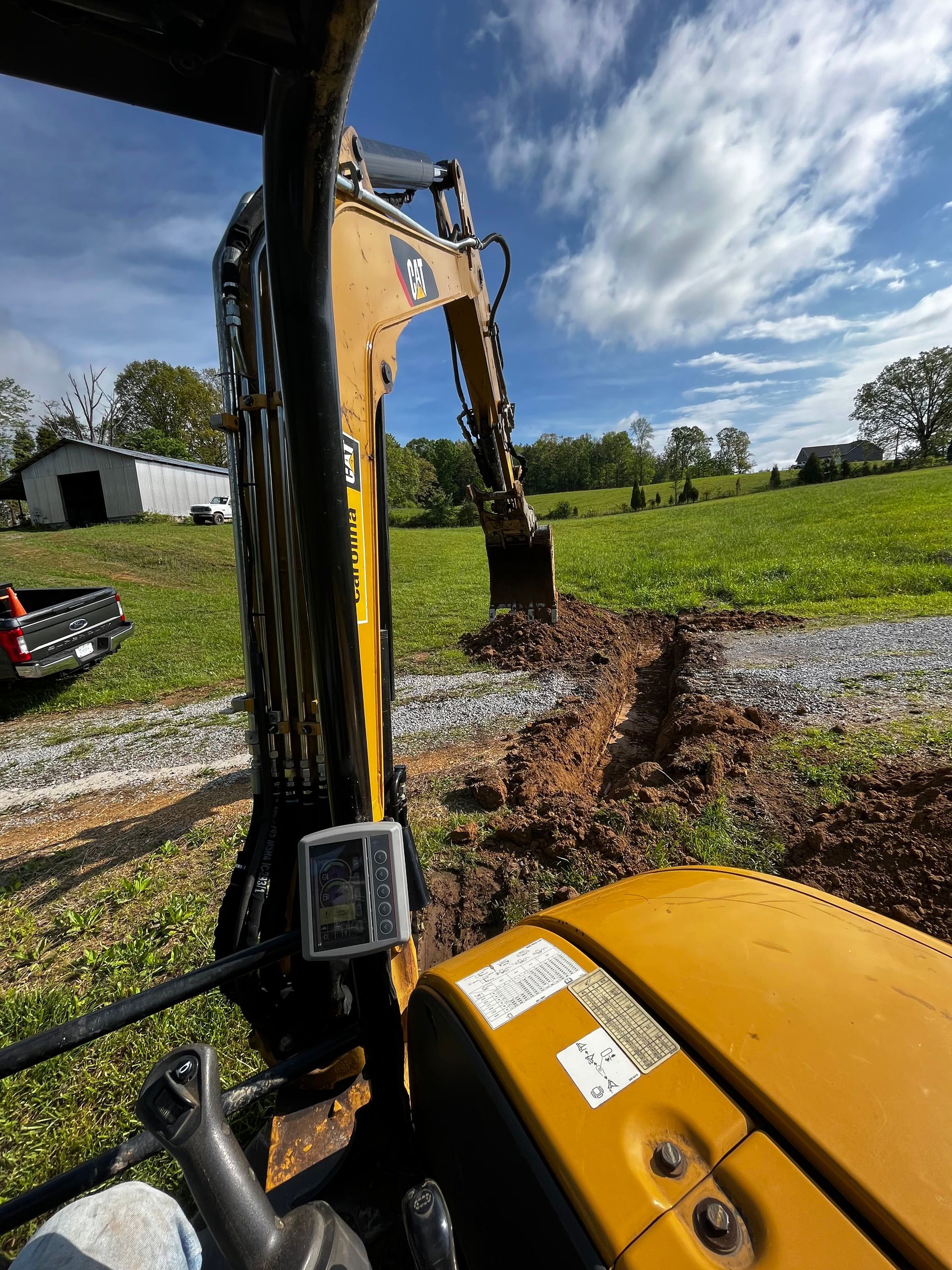 A cat excavator is digging a hole in a field