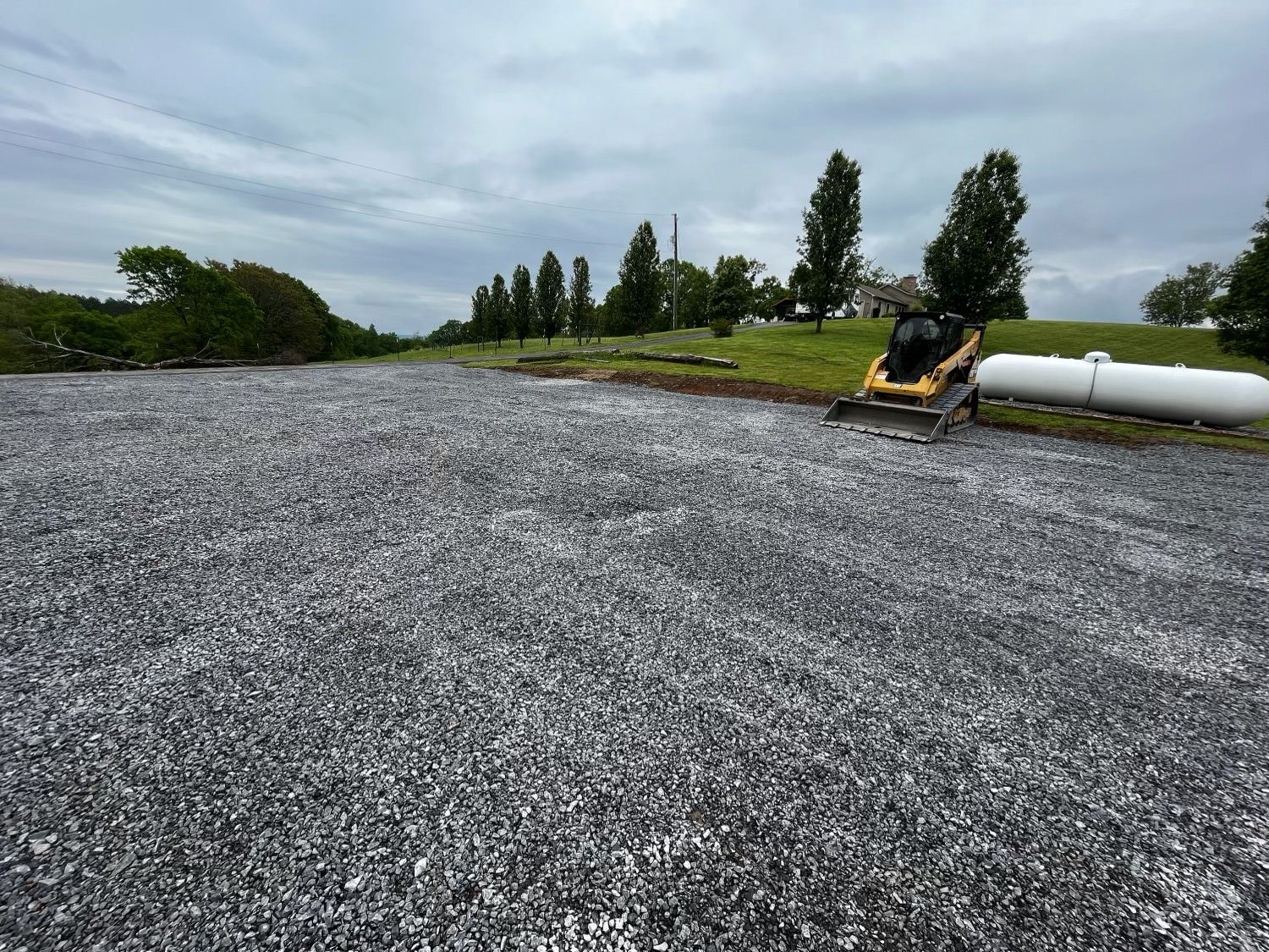 A tractor is driving down a gravel road next to a propane tank.