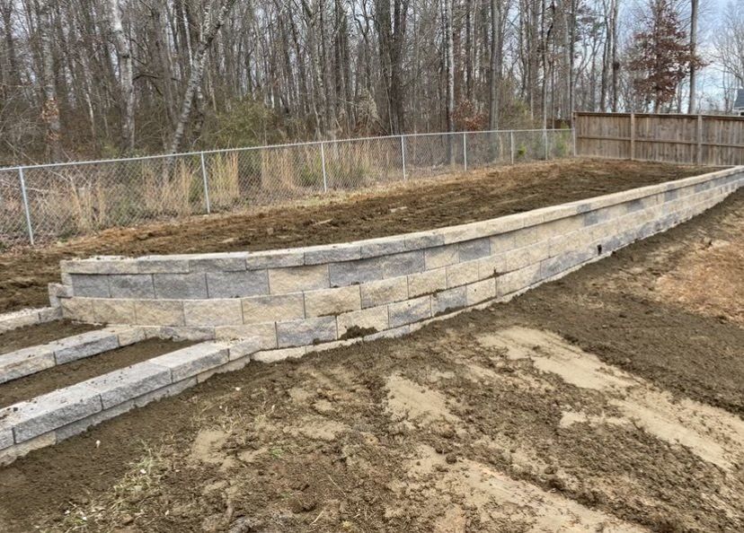 A large stone wall is sitting on top of a dirt hill next to a fence.