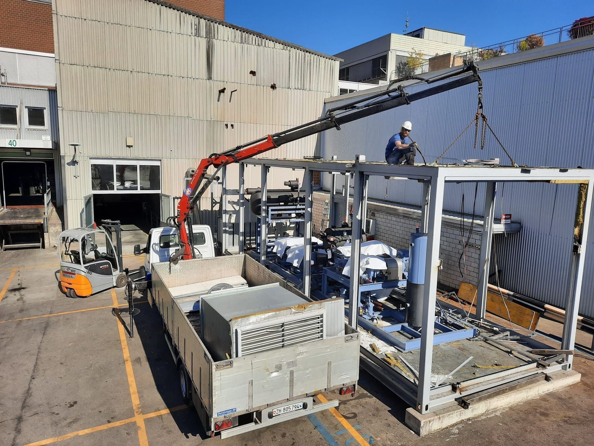 Ein Kran hebt auf einem Parkplatz eine Metallkonstruktion an.