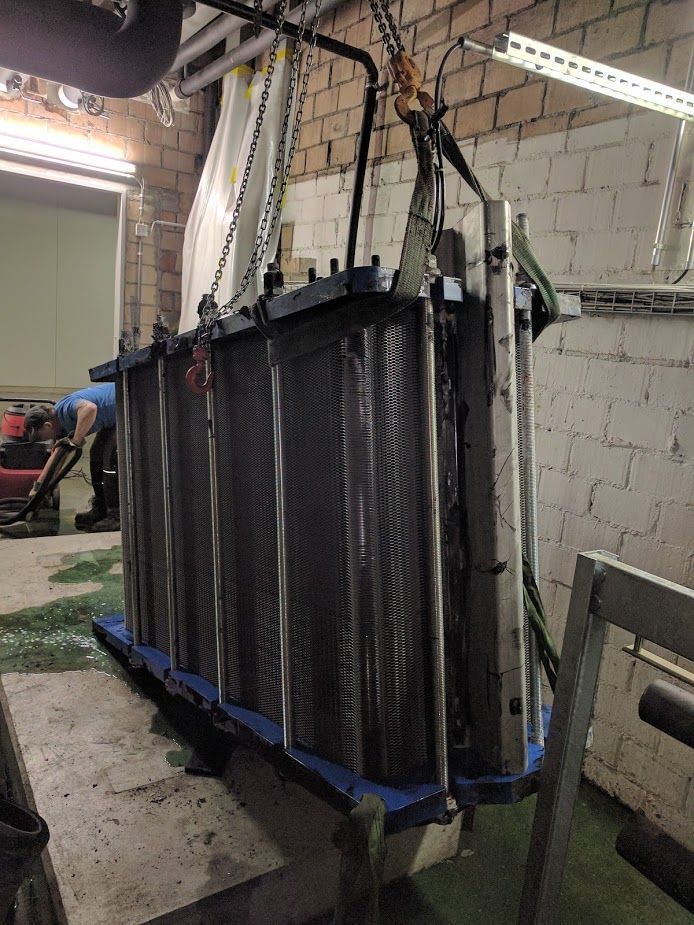 Ein großer Metallgegenstand wird mit einem Kran in einen Raum gehoben.