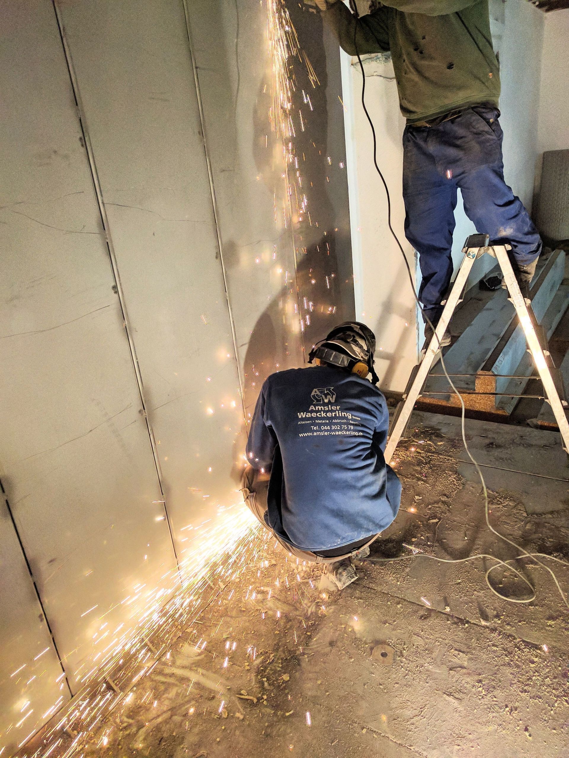 Ein Mann sitzt auf einer Leiter und schneidet ein Stück Metall.