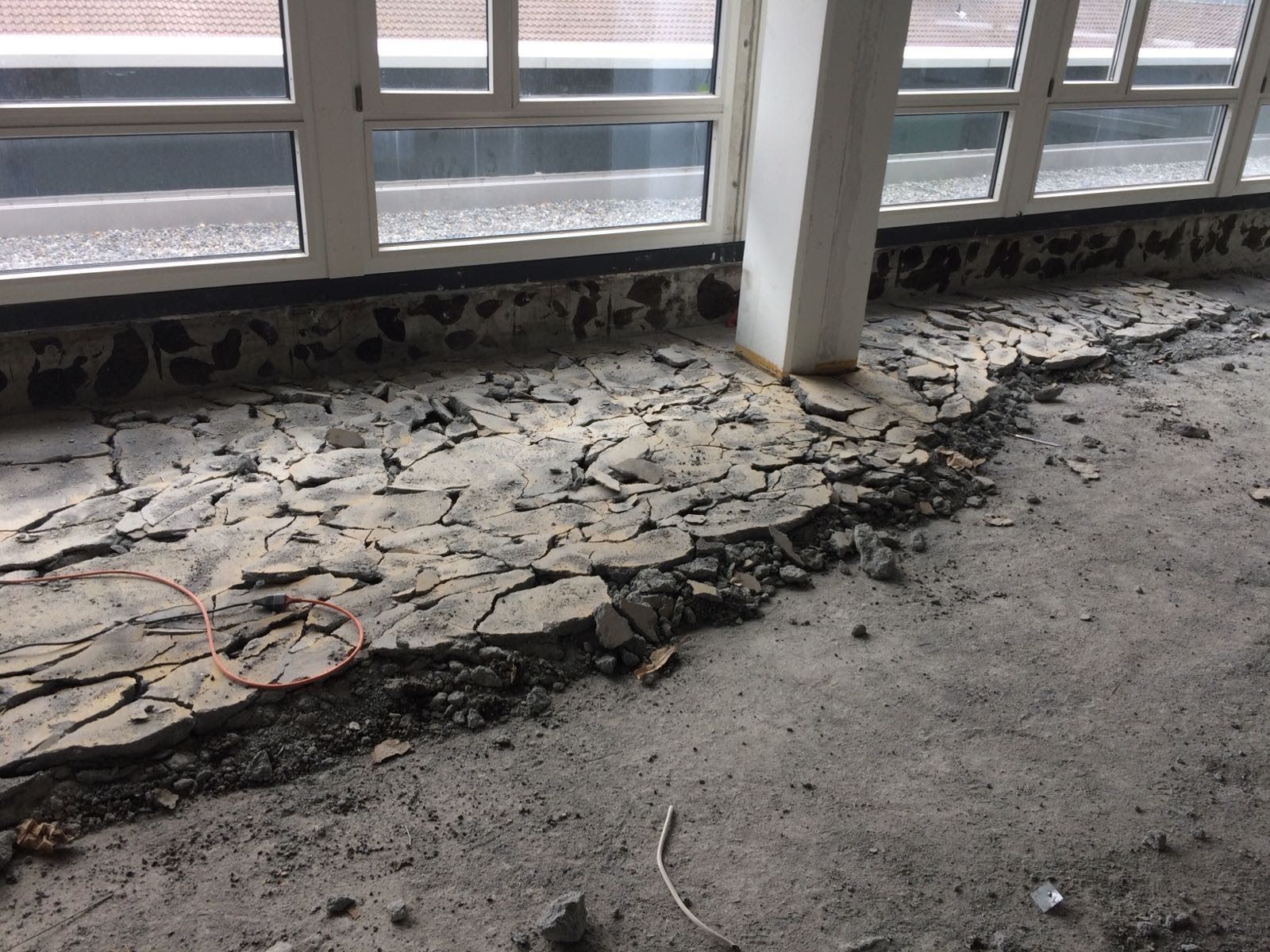 Ein Raum mit viel Beton auf dem Boden und vielen Fenstern.