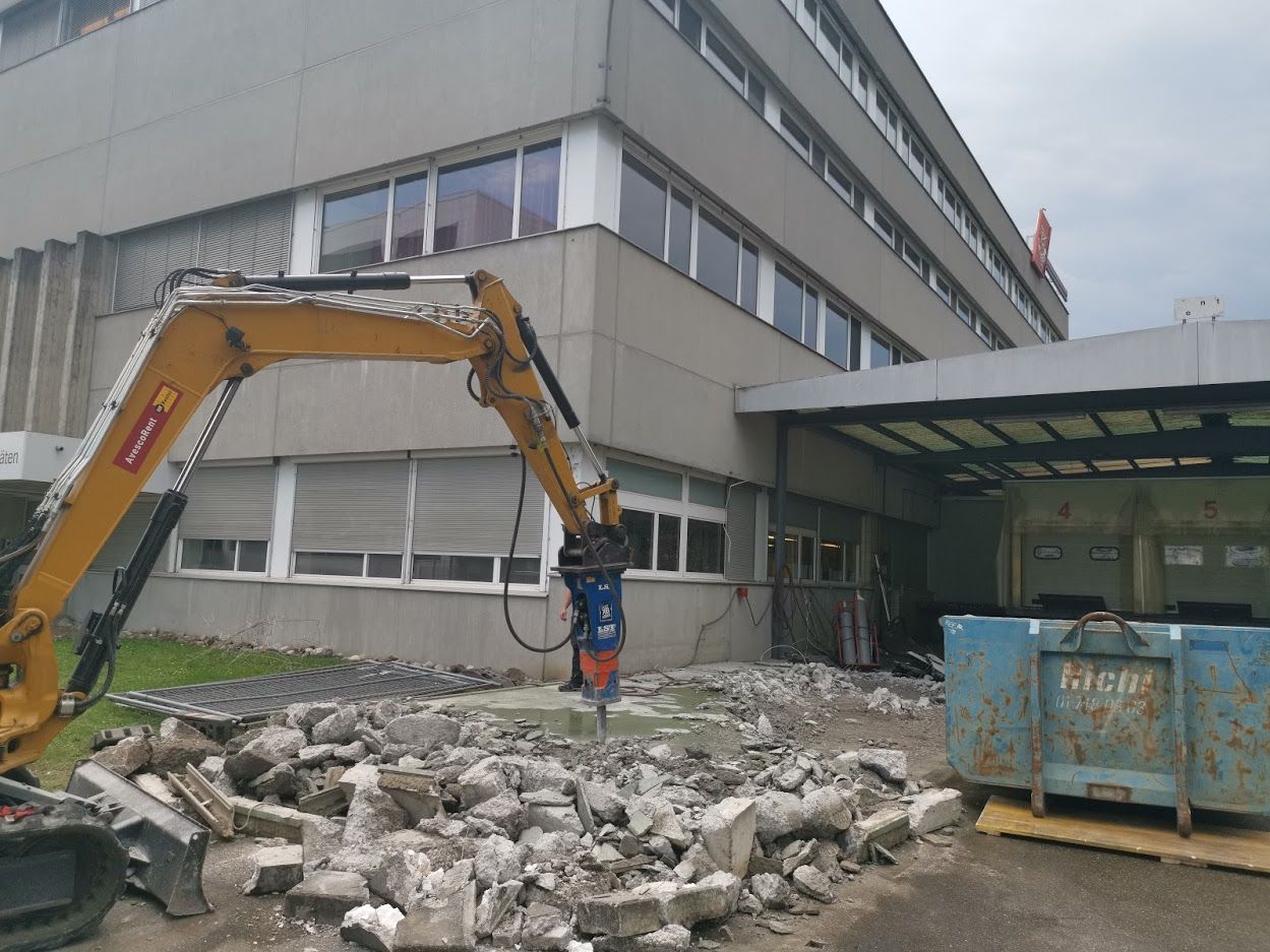 Ein großes Gebäude wird von einem gelben Bagger abgerissen.