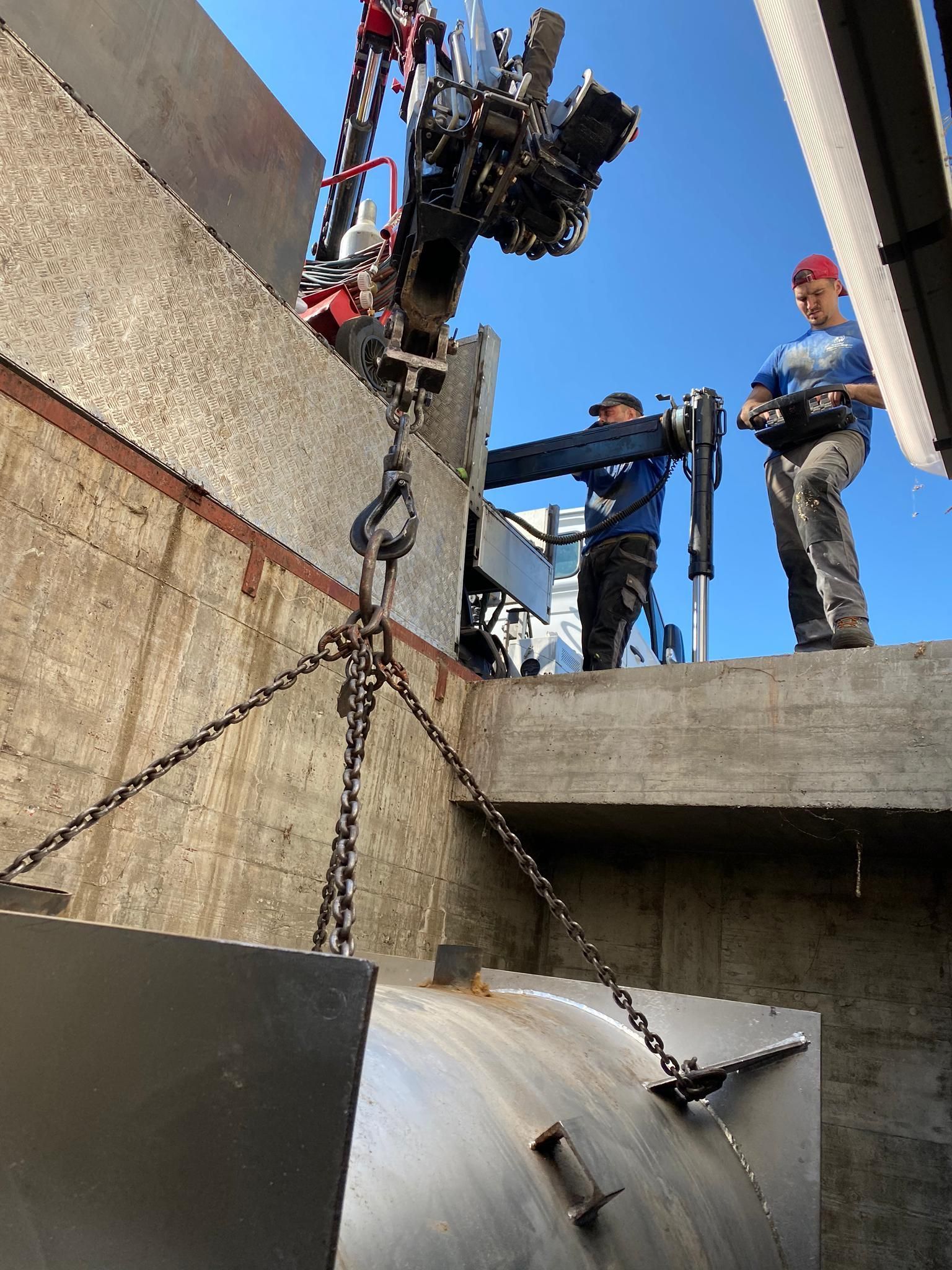 Ein Mann steht auf einer Betonmauer, während ein Kran ein großes Metallobjekt anhebt.