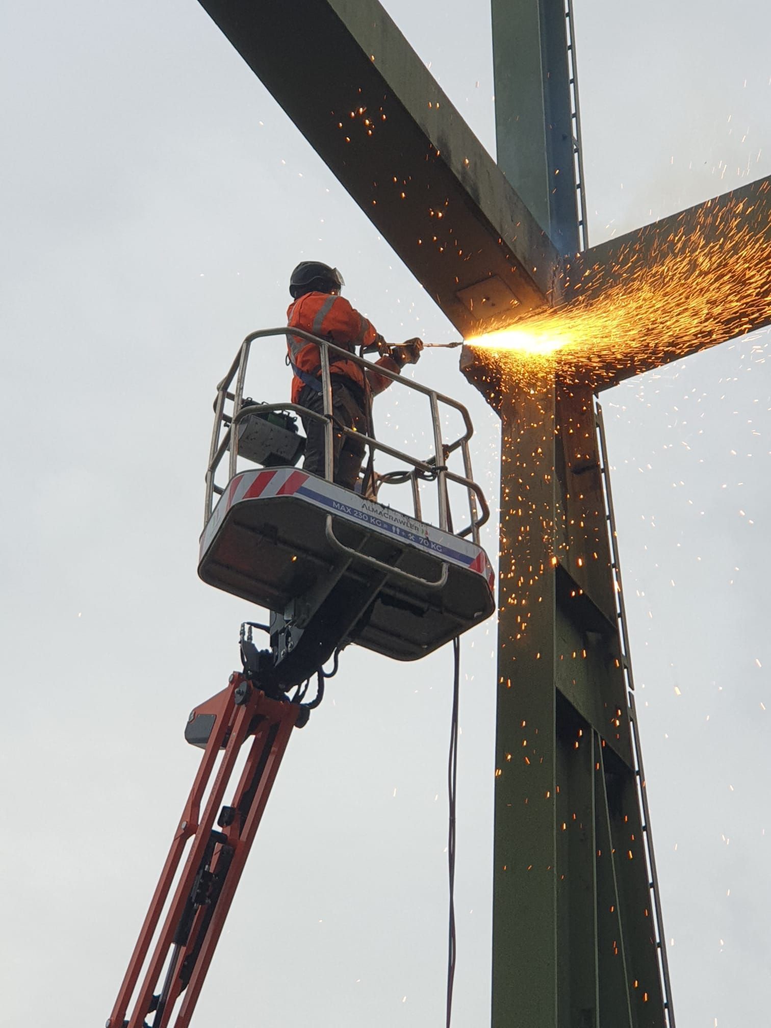 Ein Mann schneidet eine Metallstruktur mit einem Brenner, während er auf einem Lift sitzt.