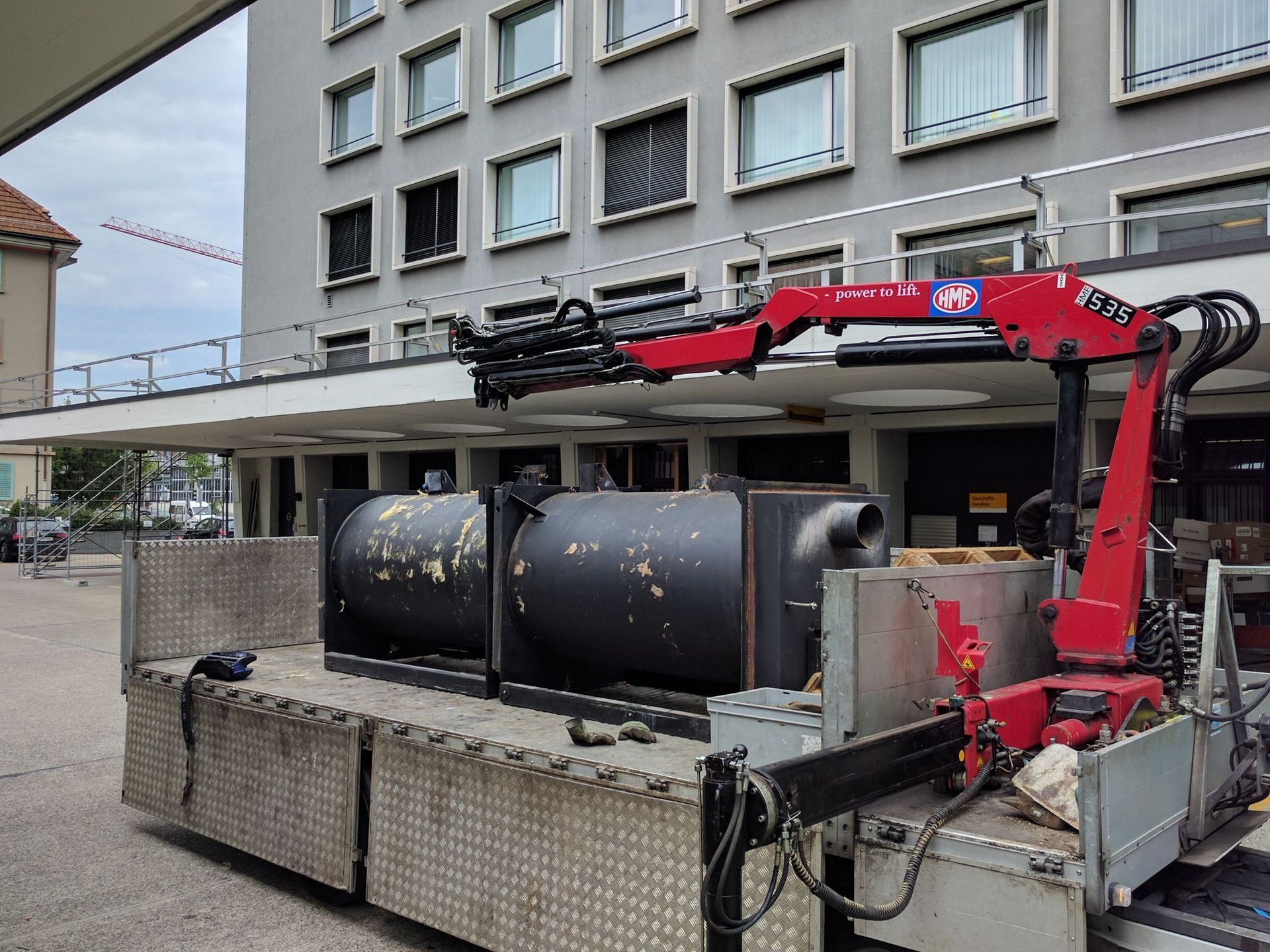 Ein LKW mit einem Kran auf der Ladefläche steht vor einem Gebäude.