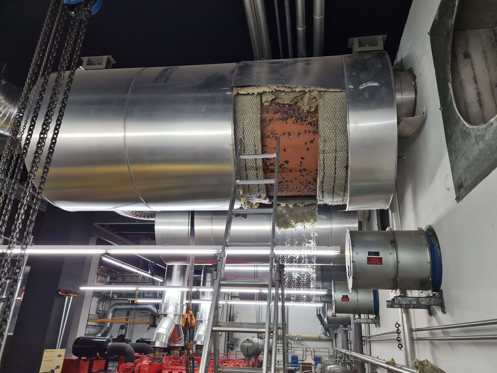 In einer Fabrik hängt eine Leiter an einem Metallrohr.