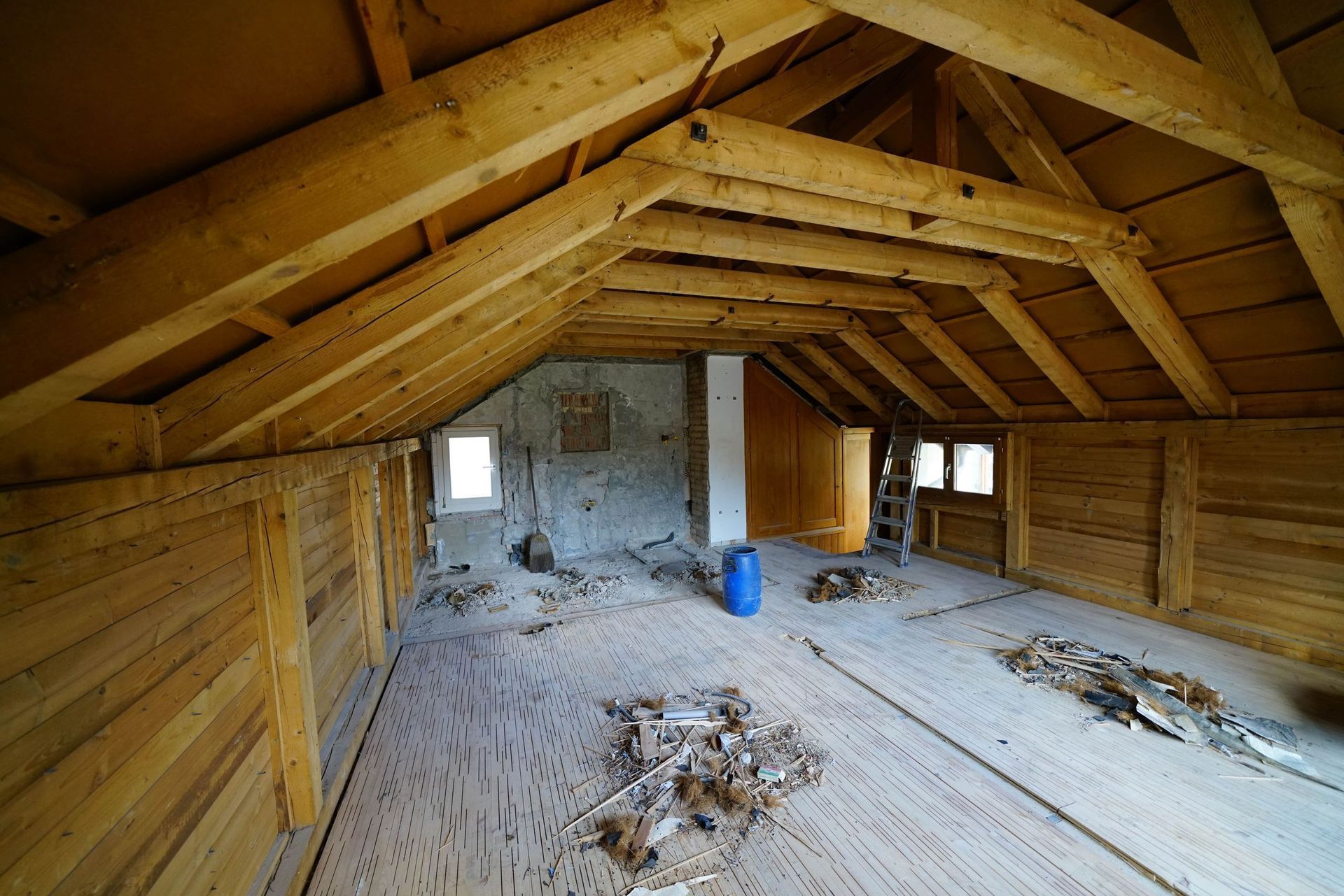 Ein leerer Dachboden mit Holzbalken und einem blauen Fass.