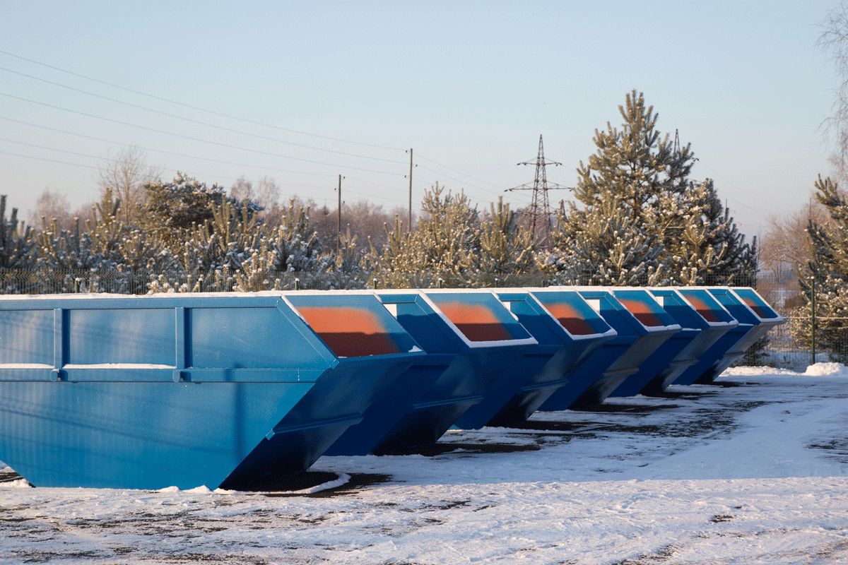 Eine Reihe blauer Müllcontainer steht im Schnee.