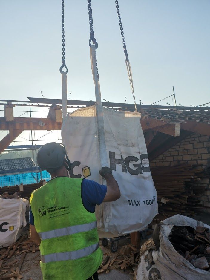 Ein Mann in einer gelben Weste hebt eine große Tasche mit der Aufschrift „HGS“ hoch.