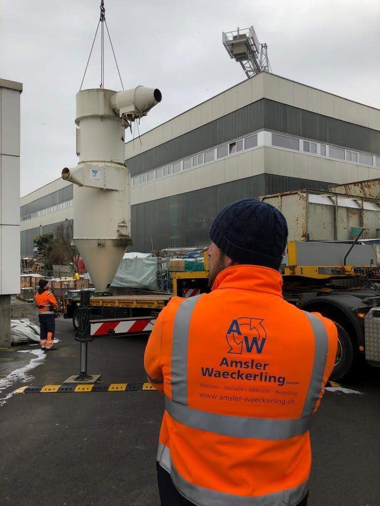 Ein Mann mit einer orangefarbenen Weste und einem A auf dem Rücken steht vor einem großen Gebäude.