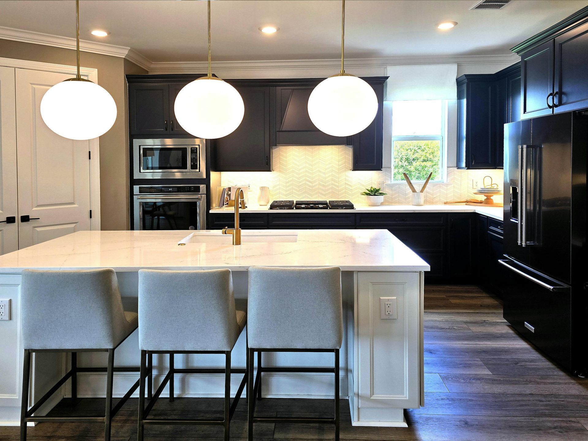 A kitchen with black cabinets , white counter tops , and a large island.
