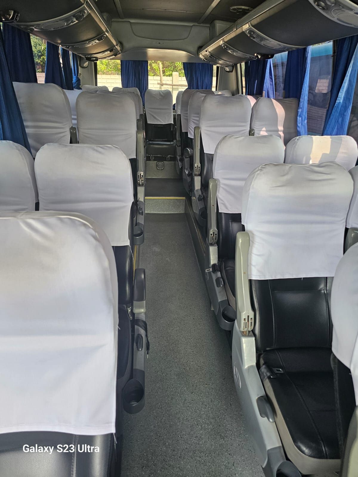 El interior de un autobús con muchos asientos y cortinas azules.