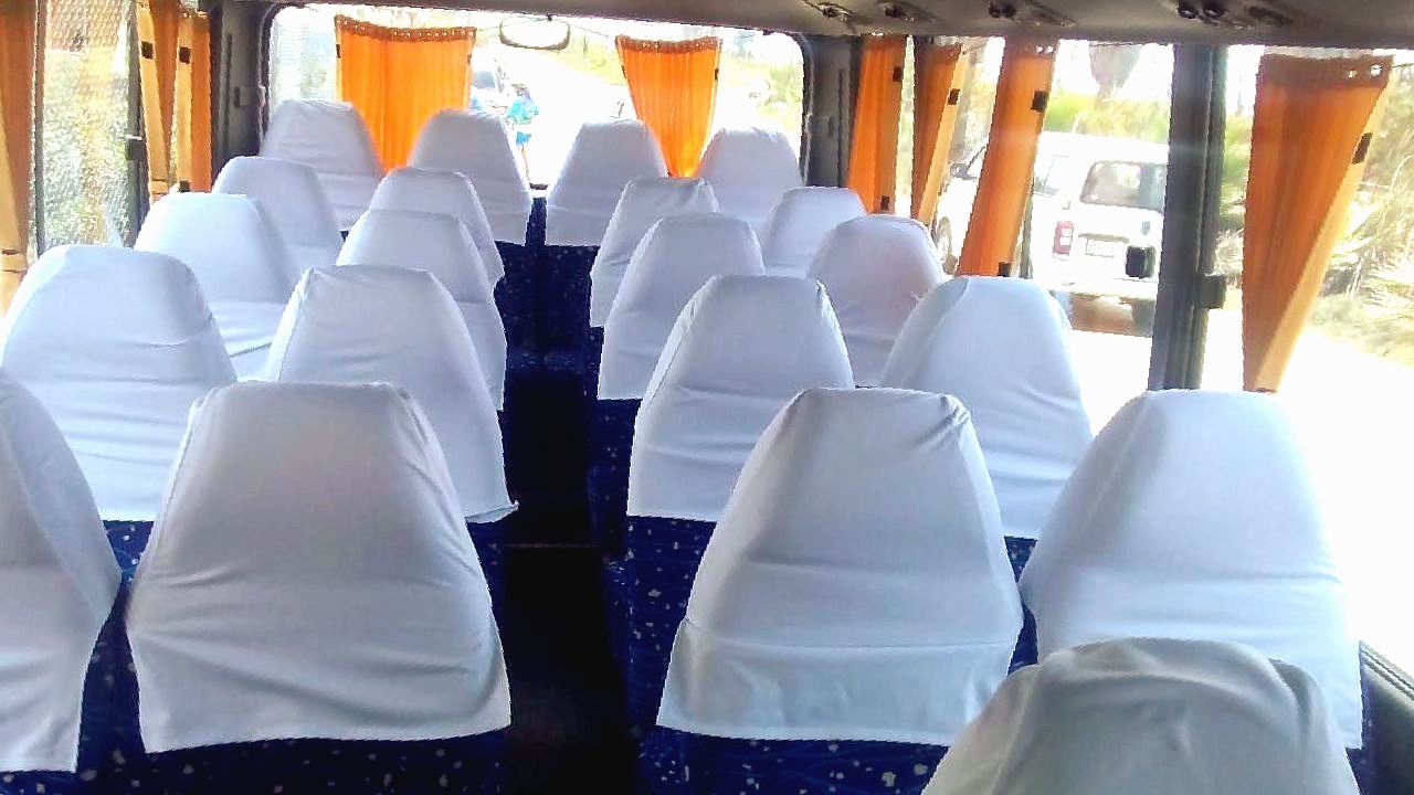 El interior de un autobús con asientos azules y fundas de asientos blancas.