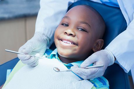 Smiling child at a dentist appointment, wearing a blue bib while gloved hands hold dental tools