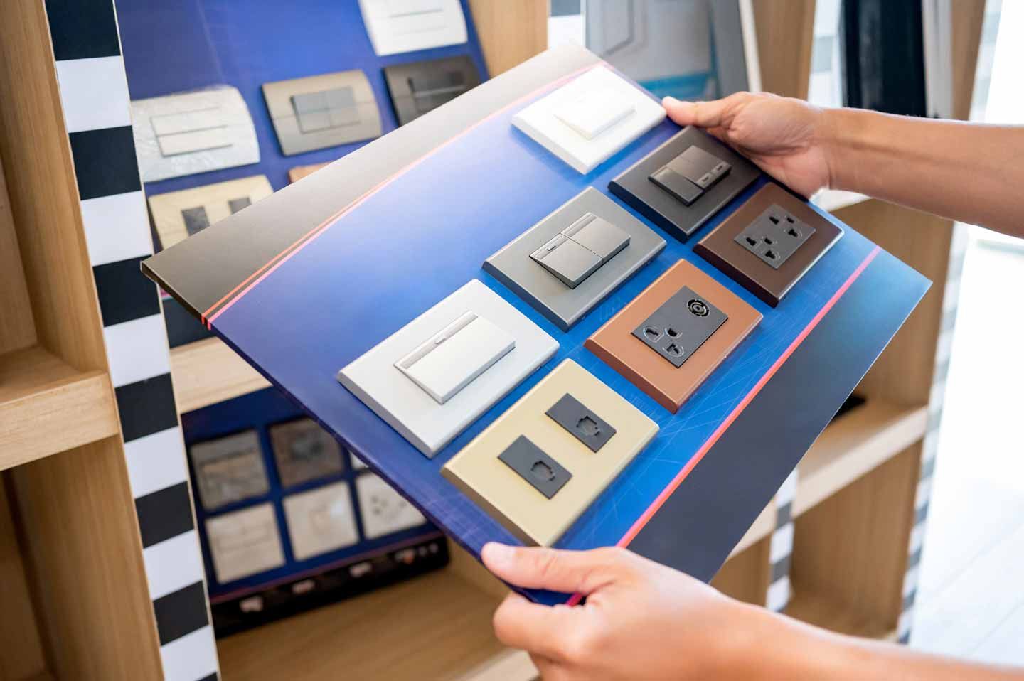 Hands holding a blue display board of light switch and outlet samples in a showroom