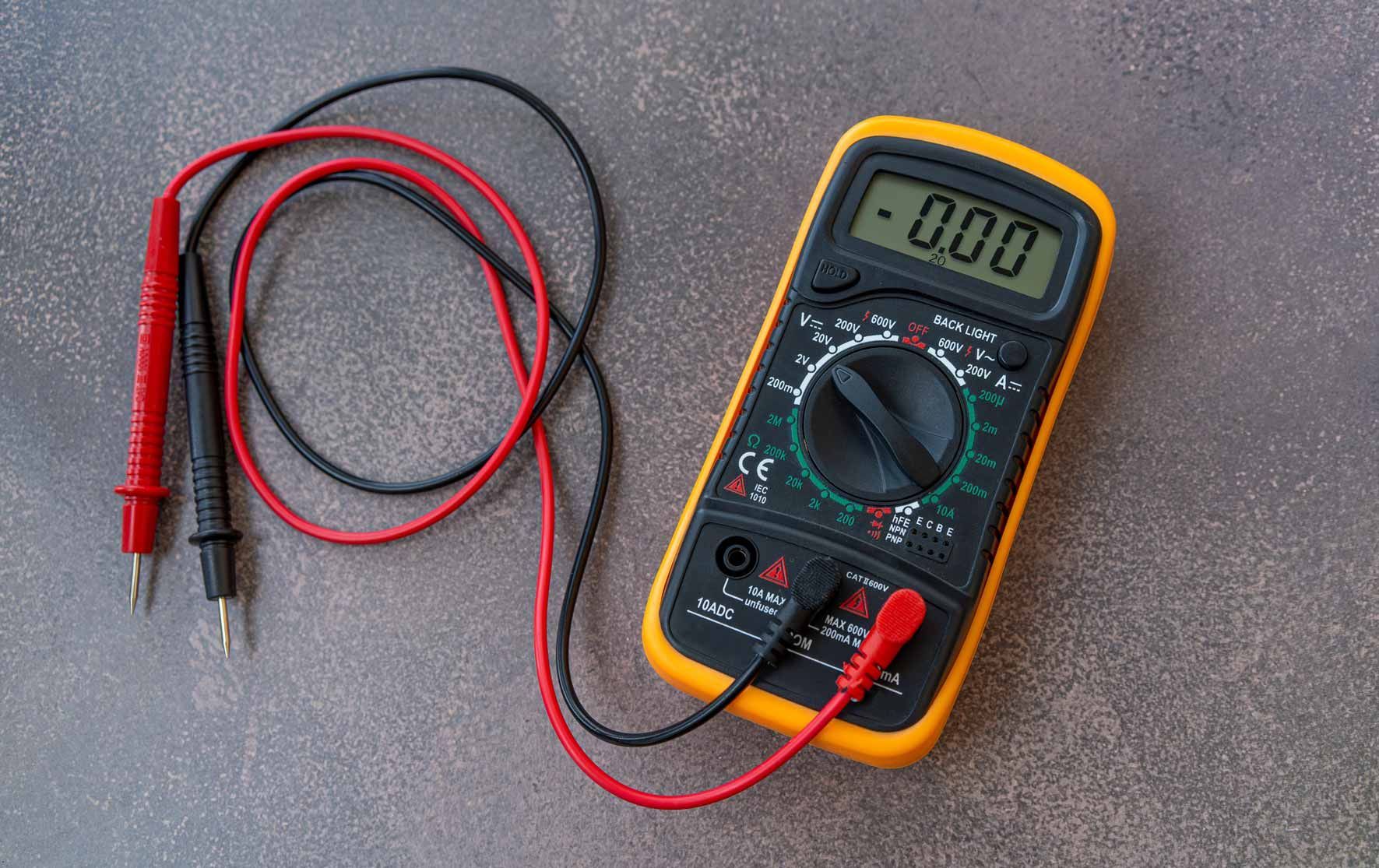 Digital multimeter with red and black test leads on a gray surface.