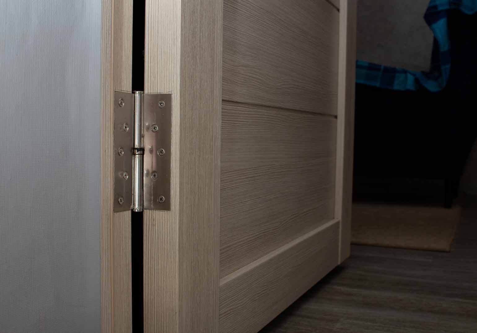 Partially open wooden door with silver hinge revealing a dark room beyond