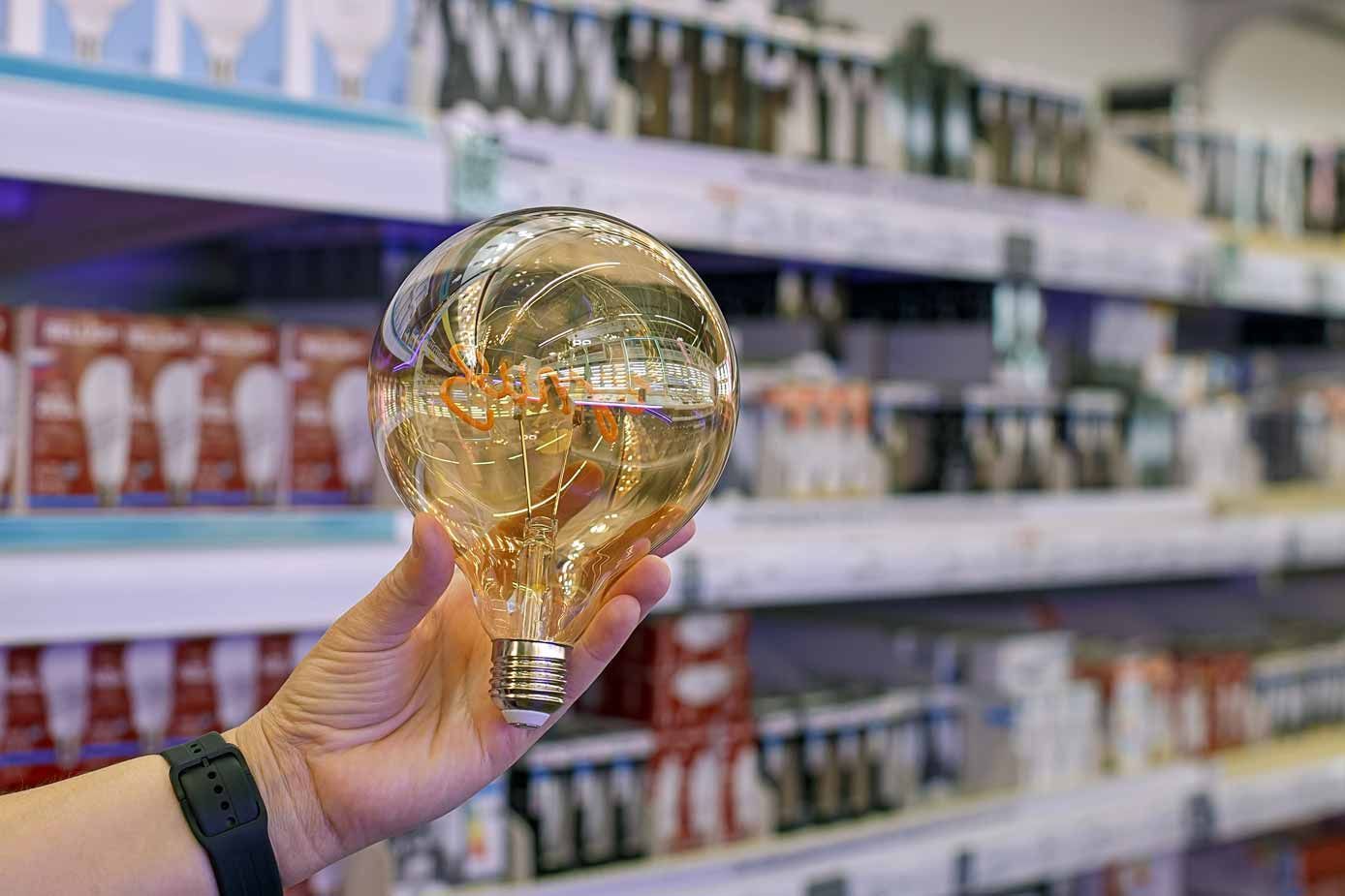 Hand holding a light bulb-shaped glass bottle in a store aisle, with blurred shelves in the background