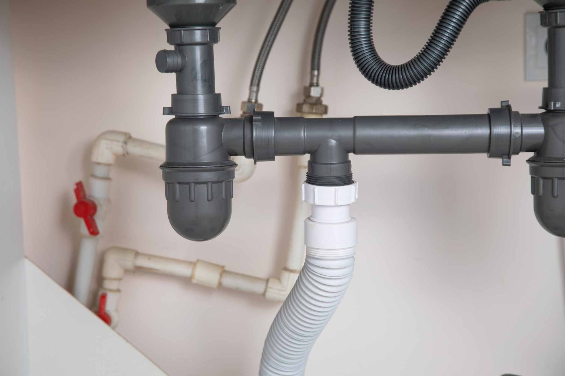 Under-sink plumbing with gray pipes, white drain hose, and a red shutoff valve